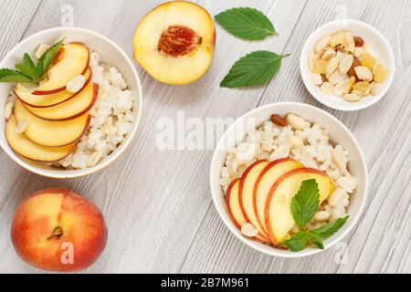 Porridge de sorgho avec morceaux de pêche, noix de cajou et amandes dans des bols en porcelaine, pêches fraîches sur des planches en bois. Salade végétalienne de sorgho sans gluten avec Banque D'Images