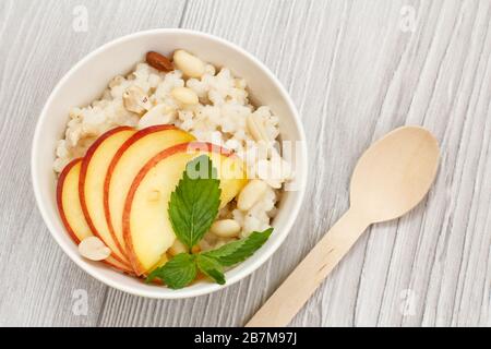 Porridge de sorgho avec morceaux de pêche, noix de cajou et amandes dans un bol en porcelaine avec cuillère sur des planches en bois. Salade végétalienne de sorgho sans gluten avec fruci Banque D'Images