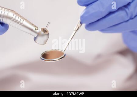 Gros plan des mains du dentiste dans des gants d'examen en latex avec miroir buccal et pièce à main dentaire à grande vitesse sur fond flou. Concept d'outils médicaux. S Banque D'Images