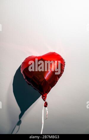 Ballon d'hélium rouge en forme de coeur avec une cravate, frappé à un plafond blanc avec ombre. Banque D'Images