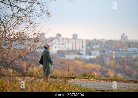 Vieille veuve marchant dans le parc de la ville d'automne. Femme solitaire regardant profondément la ville, l'auto-réflexion. Grand-mère rêvant de son concept familial. Banque D'Images