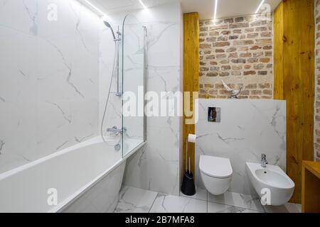 Intérieur moderne et loft de la salle de bains. Bain blanc. Mur de briques. Toilettes et bidet. Banque D'Images