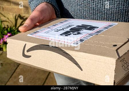 Gros plan de la personne homme transportant la livraison en ligne colis de colis de boîte Amazon avec étiquette d'avertissement de batterie lithium-ion Angleterre Royaume-Uni Banque D'Images