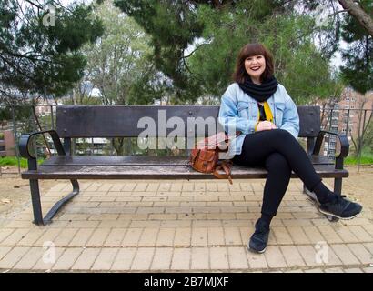 Portrait d'une jeune femme urbaine souriante et élégante en vêtements modernes et lumineux assis sur un banc. Style de vie et concept urbain. Banque D'Images