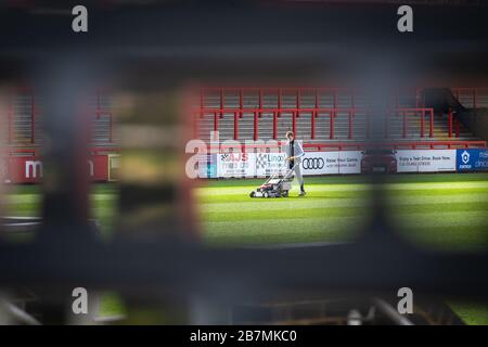 Groundsman travaillant au terrain de football coupant l'herbe, photographié à travers l'écart dans l'obturateur fermé. Banque D'Images