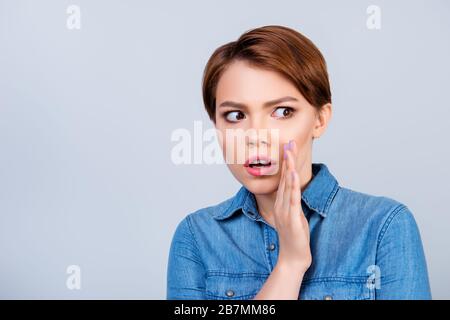 Jeune fille de cheveux rouge belle dit à quelqu'un un secret et semble choqué. Elle est vêtue d'un Jean et derrière est un fond clair Banque D'Images