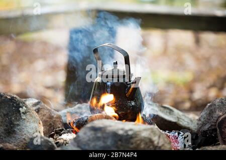 Homme et femme faisant du café dans la grande bouilloire sur feu de camp dans la forêt sur la rive du lac, faisant un feu, griller. Un couple heureux à explorer la Finlande. Scandinavie Banque D'Images