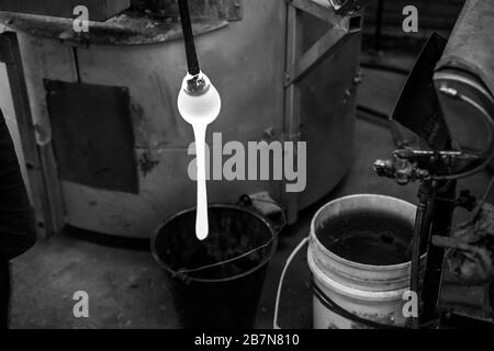 Gros plan de mise au point sélective monochrome du verre fondu qui s'écoule d'un tuyau de soufflage dans un atelier de souffleries avec espace de copie sur les côtés. Banque D'Images