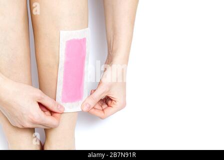 Femme utilisant des bandes de cire rose. Belle femme qui fait l'épilation pour ses jambes avec cirage, isolée sur blanc Banque D'Images