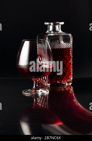 Verre de brandy et carafe sur fond sombre. Réflexion fantaisie sur un fond noir réflexive. Banque D'Images