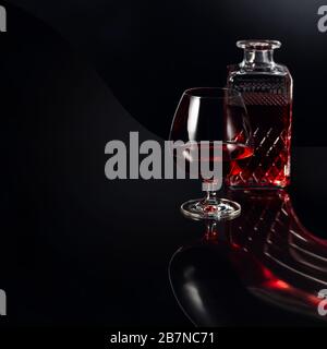 Verre de brandy et carafe sur fond sombre. Réflexion fantaisie sur un fond noir réflexive. Espace de copie. Banque D'Images