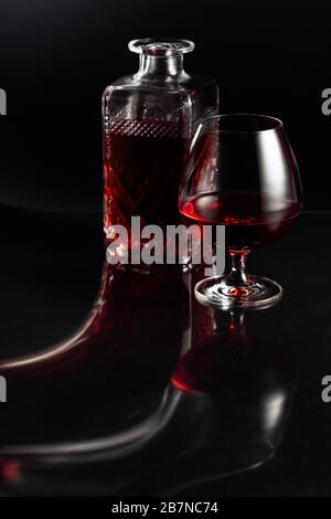 Verre de brandy et carafe sur fond sombre. Réflexion fantaisie sur un fond noir réflexive. Banque D'Images