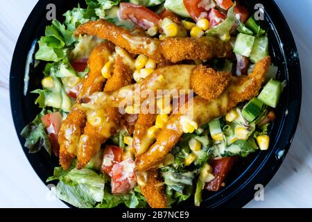 Retirez la salade cajun saine avec les doigts de poulet et la sauce moutarde dans la boîte / paquet de plaques en plastique noir. Restauration rapide bio. Banque D'Images