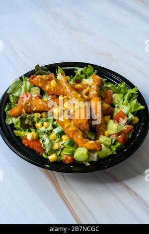 Retirez la salade cajun saine avec les doigts de poulet et la sauce moutarde dans la boîte / paquet de plaques en plastique noir. Restauration rapide bio. Banque D'Images