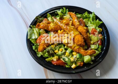 Retirez la salade cajun saine avec les doigts de poulet et la sauce moutarde dans la boîte / paquet de plaques en plastique noir. Restauration rapide bio. Banque D'Images