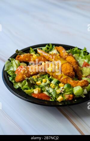 Retirez la salade cajun saine avec les doigts de poulet et la sauce moutarde dans la boîte / paquet de plaques en plastique noir. Restauration rapide bio. Banque D'Images