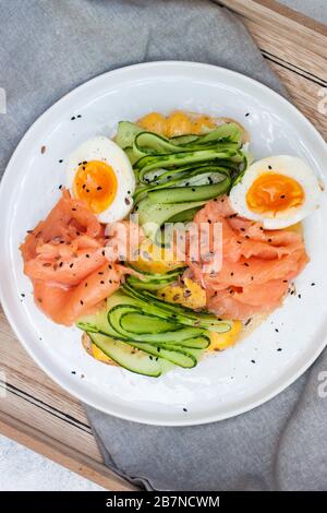 Sandwich avec pain grillé, saumon fumé, fromage à la crème, concombre en tranches et œufs durs sur plaque blanche. Banque D'Images
