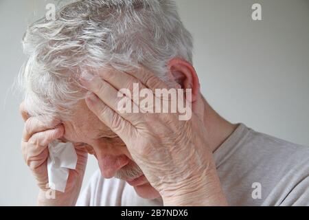 L'homme senior avec des tissus tient sa tête fiévreuse Banque D'Images