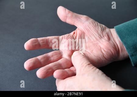 Homme senior avec une main douloureuse sur un fond gris foncé Banque D'Images
