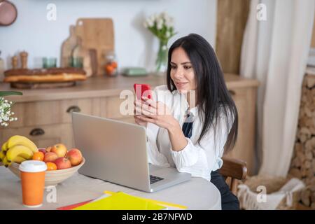 Jeune femme aux cheveux sombres qui travaille à distance et tient le téléphone dans sa main Banque D'Images