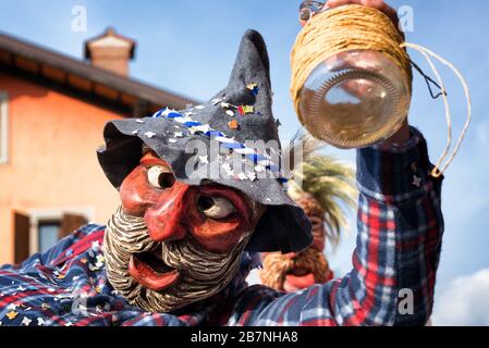 Portrait d'un homme masqué tenant une bouteille de vin vide. Heureux ivre homme en costume païen traditionnel. Défilé de carnaval de Pust. Italie. Banque D'Images