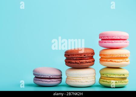 Les cookies macaroni de différentes couleurs sont disposés en forme de marches pyramidales sur un fond bleu. Banque D'Images