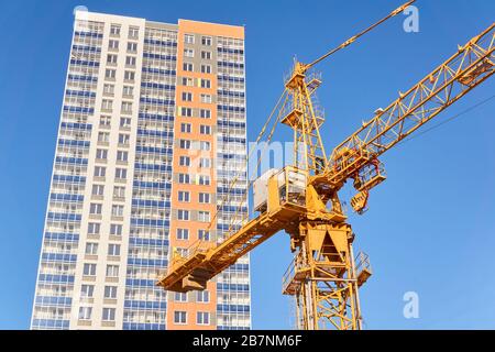 construction de plusieurs étages - cabine et flèche d'une grue de tour et la partie supérieure d'un immeuble résidentiel multi-appartement nouvellement construit contre le bleu Banque D'Images