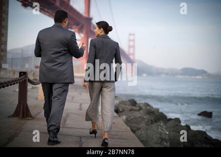 Homme d'affaires et femme d'affaires marchant le long du bord de l'eau donnant sur un port. Banque D'Images