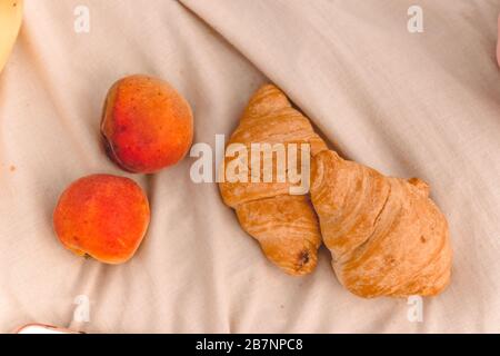 Croissants frais cuits et pêches mûres aux fruits sur un plat beige. Pique-nique d'été, vue de dessus. Banque D'Images
