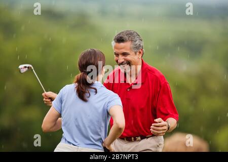 Heureux couple mûr rire ensemble car ils sont pris dans une douche de pluie soudaine sur le terrain de golf. Banque D'Images