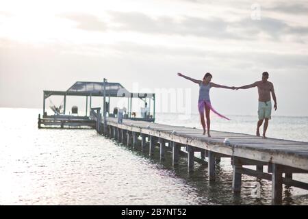 Couple en train de marcher le long d'une jetée au coucher du soleil Banque D'Images