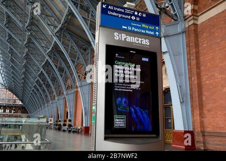 Comme le gouvernement britannique a demandé instamment à tous les Britanniques d'éviter les voyages non essentiels à l'étranger pour lutter contre la pandémie de Coronavirus en Grande-Bretagne, les passagers ferroviaires passent par une annonce numérique d'information publique du gouvernement et le NHS (National Health Service) dit au public de se laver les mains soigneusement, Dans un hall exceptionnellement calme de la gare de St Pancras, le terminus de Londres pour les services Eurostar vers l'Europe continentale, le 17 mars 2020, à Londres, en Angleterre. Banque D'Images