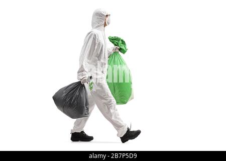 Photo en profil sur toute la longueur d'un homme portant un costume de protection et marchant avec des sacs de déchets isolés sur fond blanc Banque D'Images