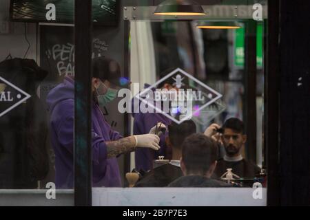 Bethenal Barber, Londres, Royaume-Uni. 17 mars 2020. Un coiffeur coupe les cheveux dans un masque de protection et des gants en caoutchouc à Bethenal Green. De nouveaux cas et décès résultant de la souche COVID-19 du Coronavirus continuent d'être signalés quotidiennement au Royaume-Uni avec des appareils sportifs majeurs annulés et les gens ont conseillé de rester à la maison s'ils ont une toux et une température élevée. Crédit: Marcin Nowak/Alay Live News Banque D'Images