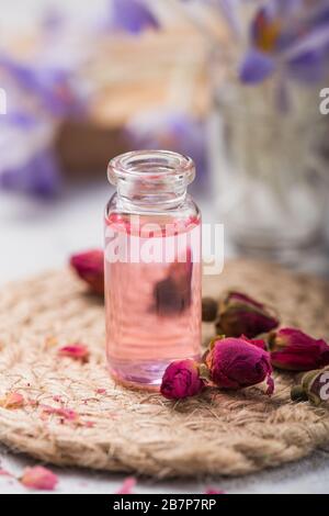 L'huile de rose pure naturelle ou l'eau parfumée dans des bouteilles pour le spa, les soins de la peau ou l'aromathérapie avec des roses roses sèches. Concept de cosmétiques organiques. Mise au point sélective Banque D'Images