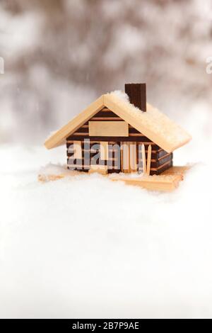 Petit modèle de maison en bois parmi les chutes de neige avec fond de forêt d'hiver flou Banque D'Images