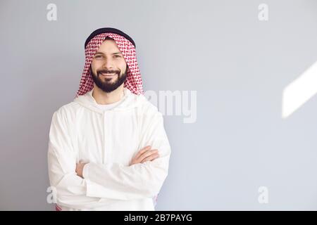 Un homme arabe souriant et séduisant a traversé les bras sur un fond gris Banque D'Images