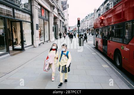 Deux enfants marchent le long d'une rue exceptionnellement calme Regent's Street, Londres, Royaume-Uni portant des masques de visage pendant la pandémie du virus corona. 17 mars 2020. Banque D'Images