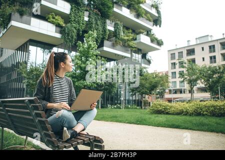 La fille sur le banc utilise un ordinateur portable. Elle est un indépendant ou blogger ou redacteur publicitaire. Elle est étudiante, peut-être travailler à distance Banque D'Images