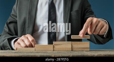 Homme d'affaires faisant un escalier comme la structure des chevilles en bois dans une image conceptuelle du progrès et de la promotion des affaires. Banque D'Images