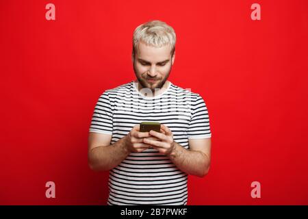 Blonde a embourbé un jeune caucasien discutant avec quelqu'un en utilisant un téléphone sur un fond rouge Banque D'Images