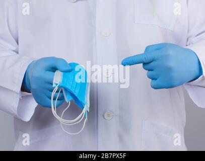 médecin en manteau blanc, les gants stériles en latex bleu contiennent des masques médicaux en textile dans sa main, un accessoire de protection contre les virus et les bactéries, gros plan Banque D'Images