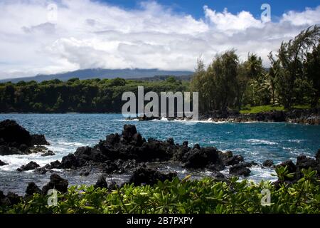 Littoral de lave Rocky avec océan, feuillage vert, et montagnes s'élevant à distance à Hawaï. Banque D'Images
