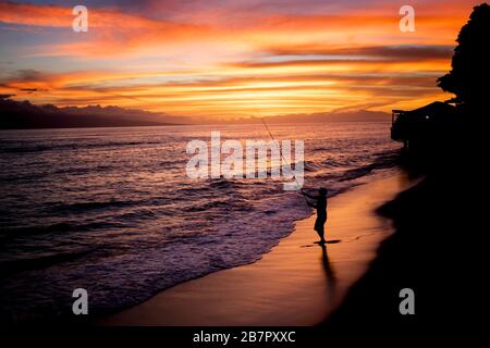 L'homme en silhouette se pêche alors que le soleil se couche sous l'horizon sur l'île tropicale. Banque D'Images