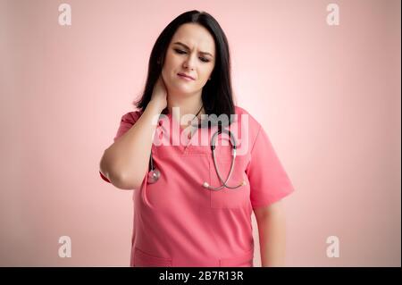 Portrait de belle femme médecin avec stéthoscope portant des gommages roses, avec des bras ouverts regardant vers le haut, a mal de gorge se posant sur un backroun isolé rose Banque D'Images