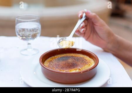 Une main féminine tient une grande cuillère de crème sautée dessert avec un verre d'eau gazeuse dans un café extérieur. Banque D'Images