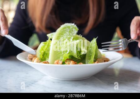 Gros plan image d'une femme mangeant une salade césar par couteau et fourchette sur table dans le restaurant Banque D'Images