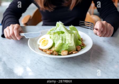 Gros plan image d'une femme mangeant une salade césar par couteau et fourchette sur table dans le restaurant Banque D'Images