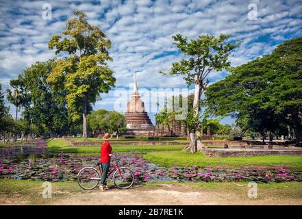 Woman in red shirt équitation location près de l'ancien temple bouddhiste en parc historique de Sukhothai, Thaïlande Banque D'Images