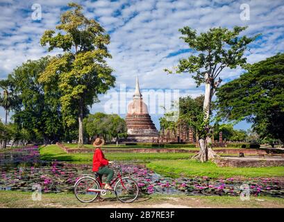 Woman in red shirt équitation location à à l'ancien temple bouddhiste en parc historique de Sukhothai, Thaïlande Banque D'Images
